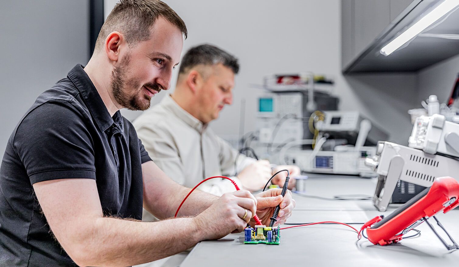 Dwaj technicy w laboratorium elektronicznym, wykonujący precyzyjne zadania montażowe w odpowiednich warunkach oświetleniowych