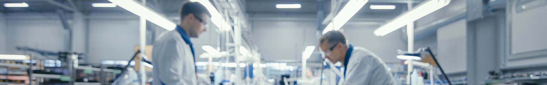 Dwóch mężczyzn w fartuchach laboratoryjnych pracuje w nowoczesnym laboratorium przy produkcji elektroniki