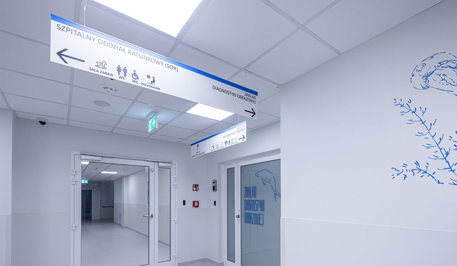 Korytarz w placówce ochrony zdrowia z wyraźnymi znakami na ścianach, ułatwiającymi poruszanie się pacjentom i pracownikom